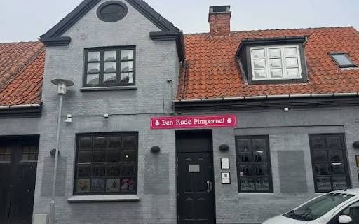 Den Røde Pimpernel i Kerteminde: et gråt hus med rødt tegltag og navnet på et rødt skilt over døren