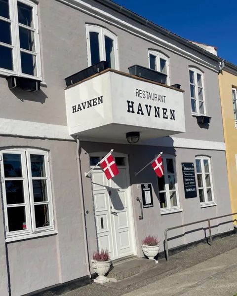 Restaurant Havnen i Kerteminde: et lysegråt hus med navnet på altanen og to dannebrogsflag ved døren